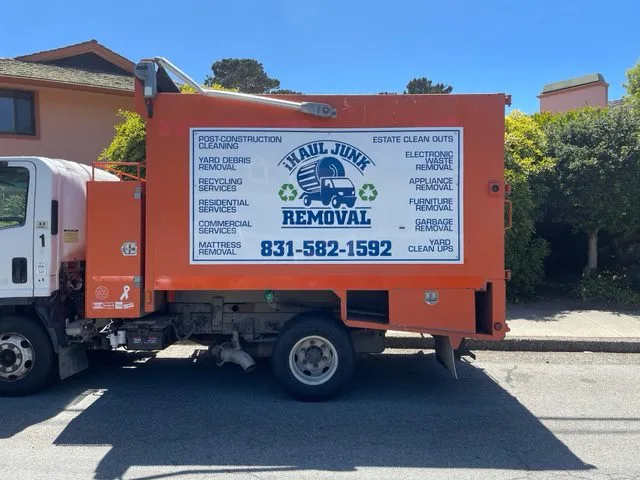A white and orange Haul Junk removal truck parked on a street with residential buildings in the background.